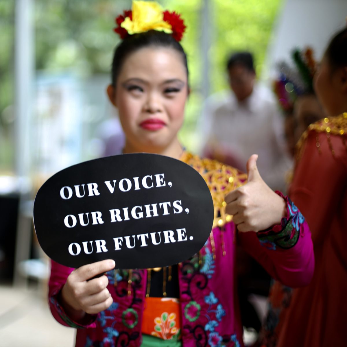 A smiling young woman holds a sign: Our Voice. Our Rights. Our Future.