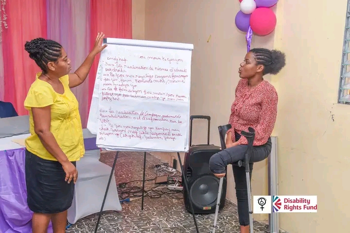Two Haitian women are looking at a Flipchart inside a room.