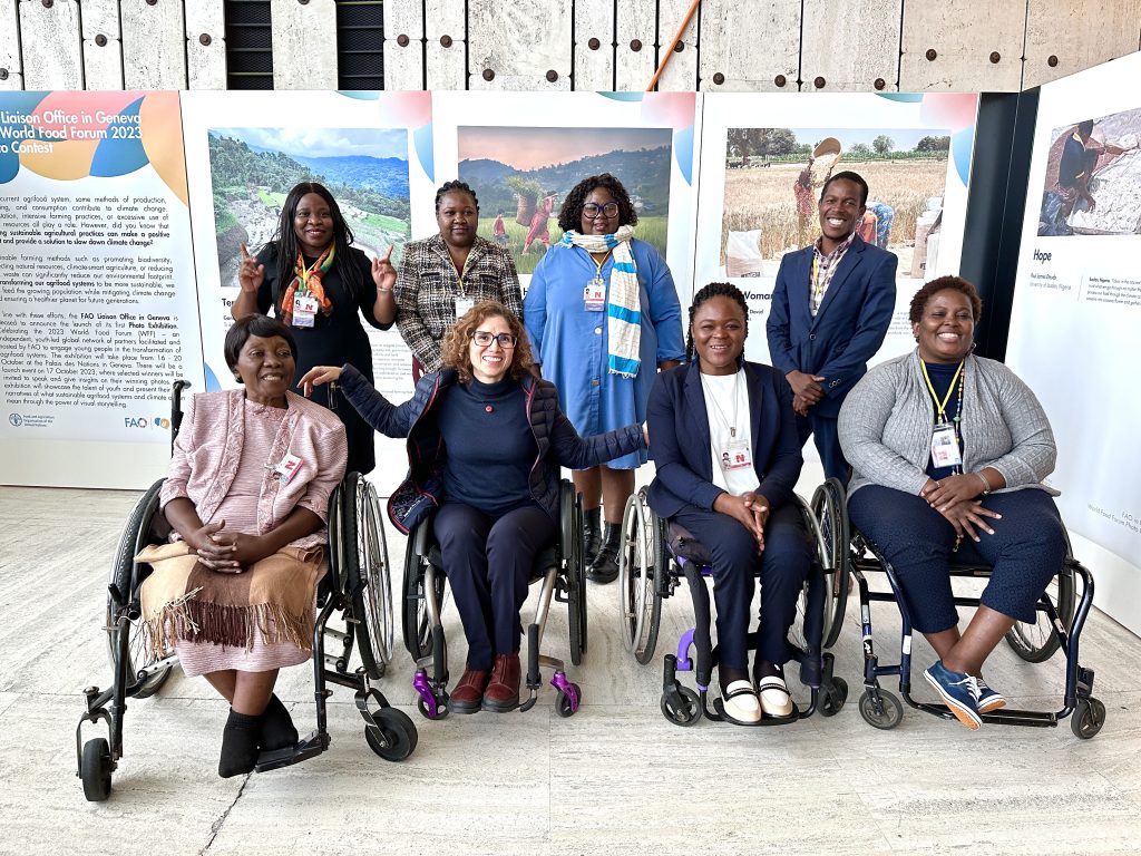 Seven smiling women and a man are standing in front an exhibit.